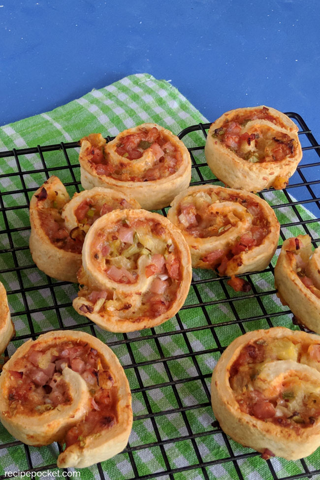 Oven baked ham and cheese pinwheels cooling on a cake rack.