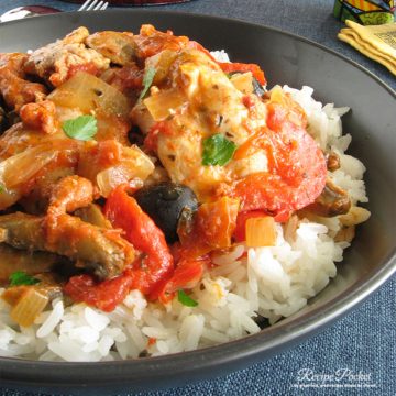 Chicken thighs in tomato sauce on rice in a bowl.
