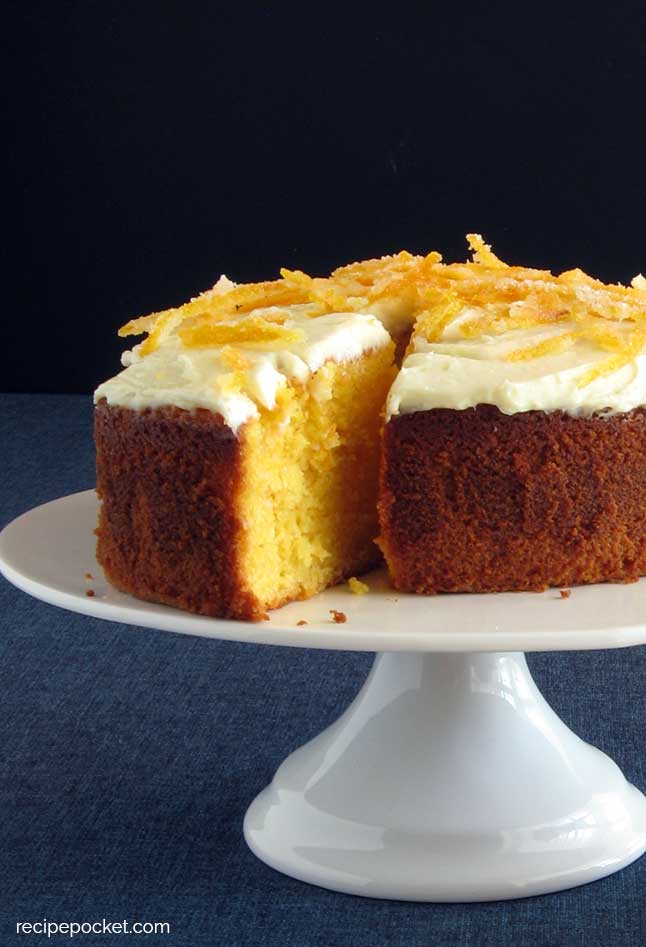 Image of showing this easy fresh orange juice cake on a white cake stand against a black background..