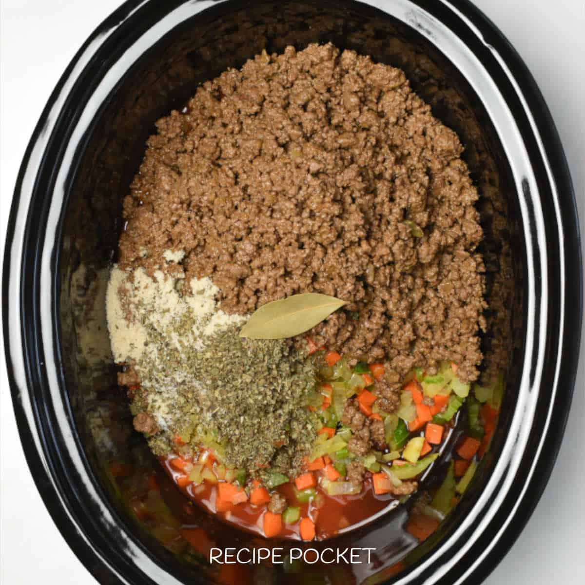 Bay leaf and dried herbs in a slow cooker with ground beef and vegetables.