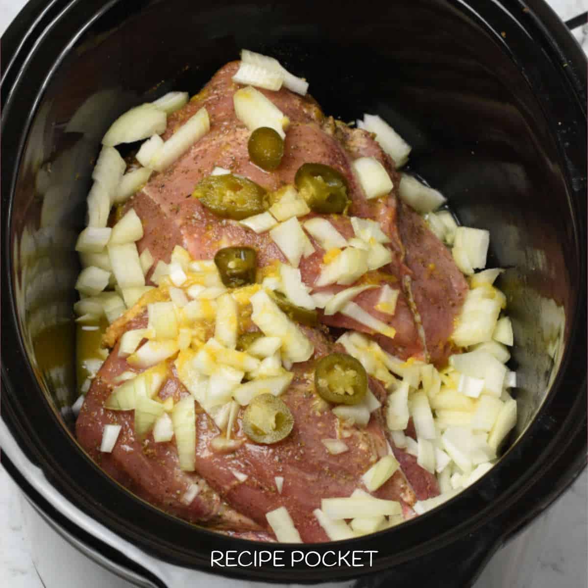 Pork shoulder in a slow cooker with onions and jalapenos.