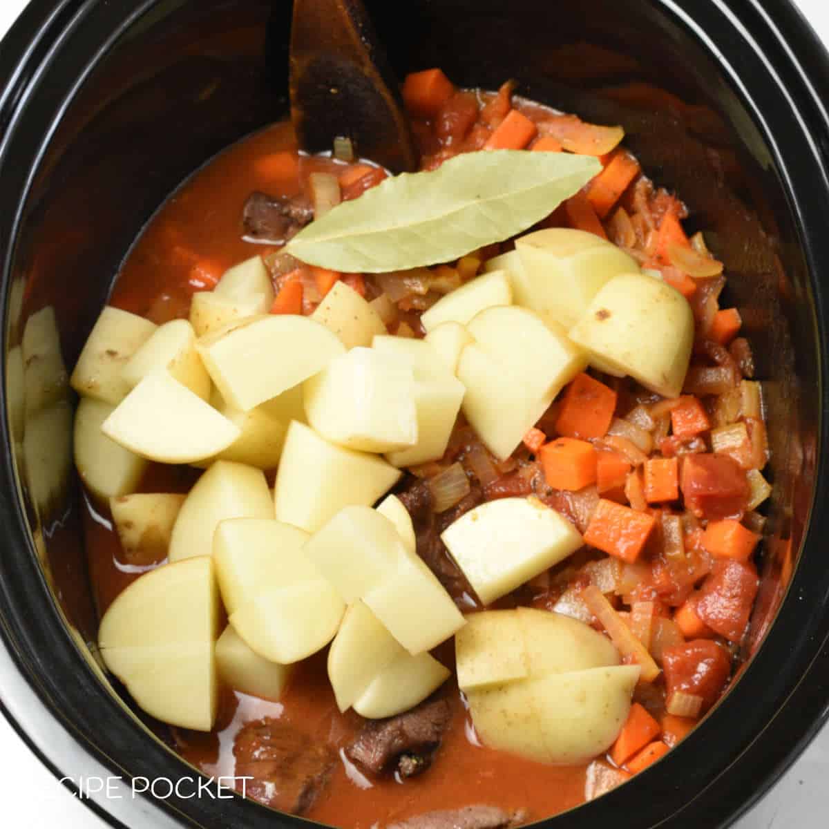 Potatoes, bay leaf, and other ingredients in a slow cooker bowl.