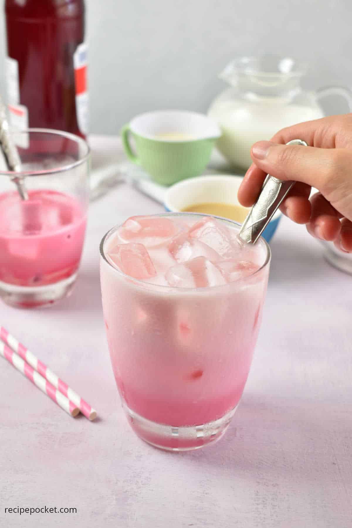 A glass of pink milk being stirred.