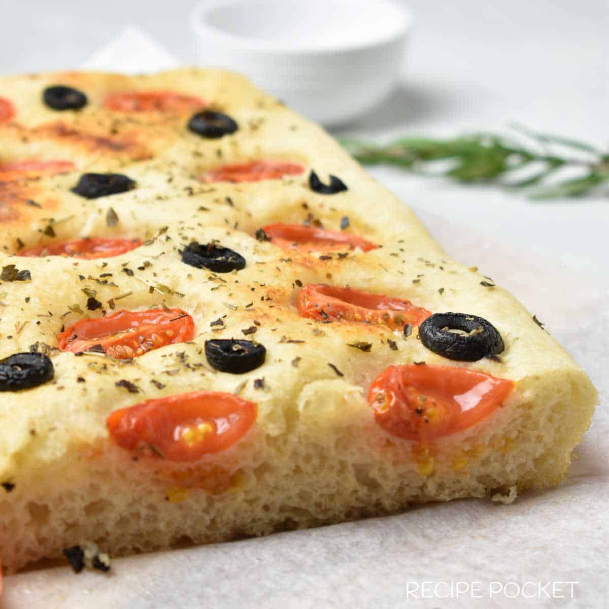Focaccia bread with a sprig of rosemary in the background.