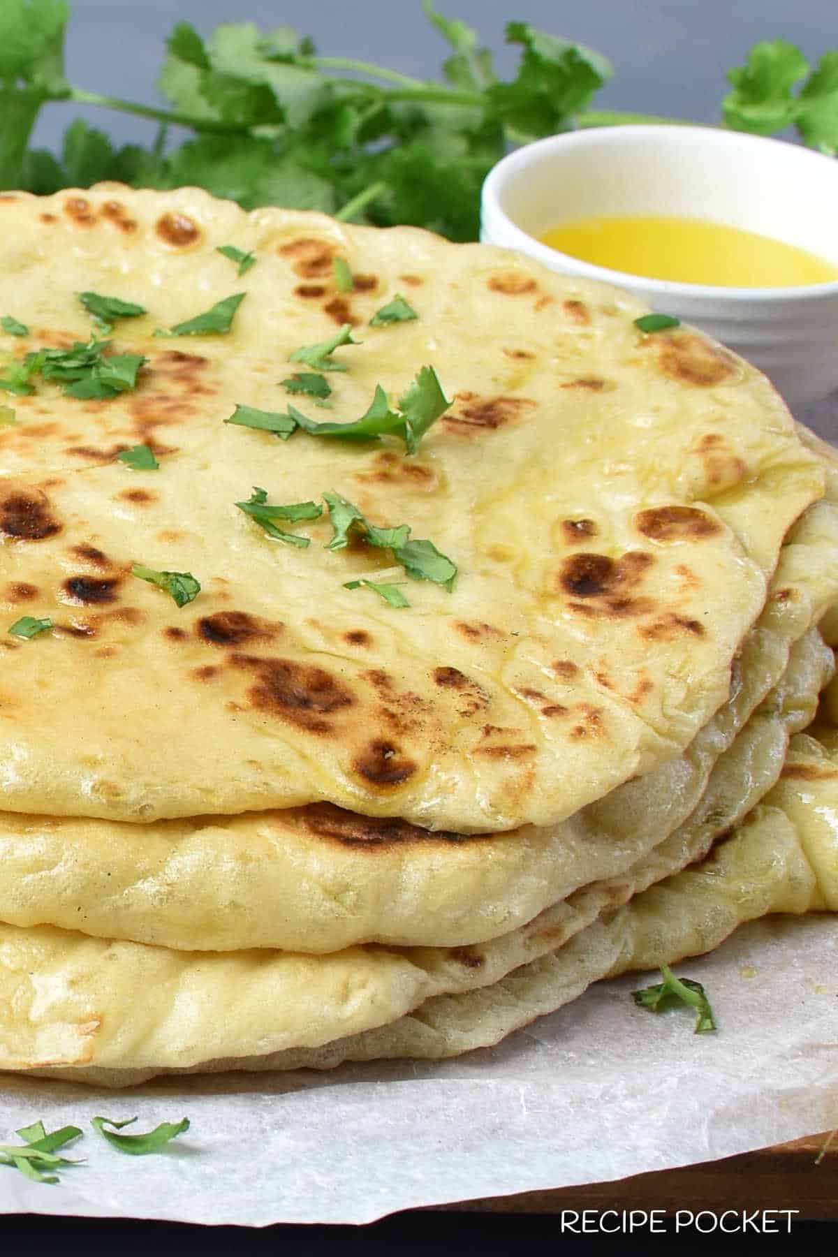 A closeup of naan bread brushed with butter and garnished with chopped coriander.