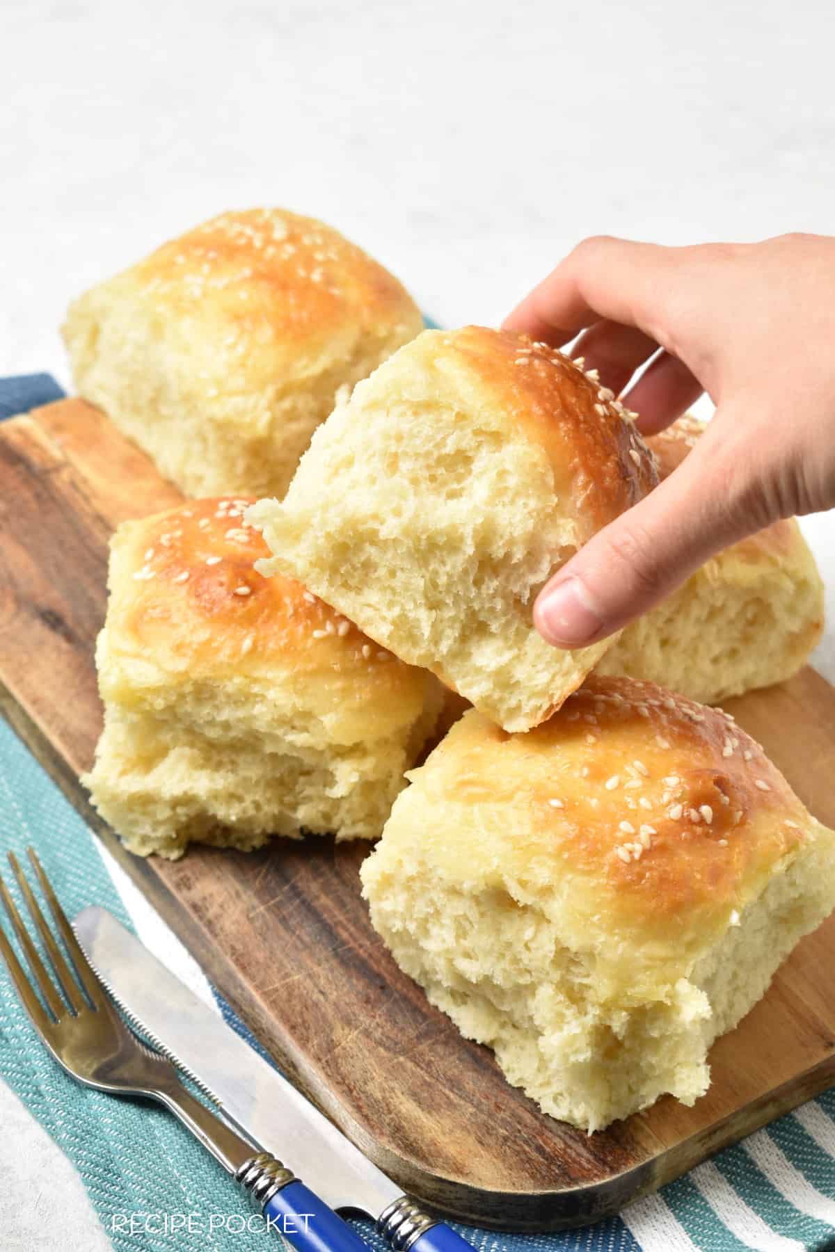 Dinner rolls on a cutting board with a hand picking up a roll.