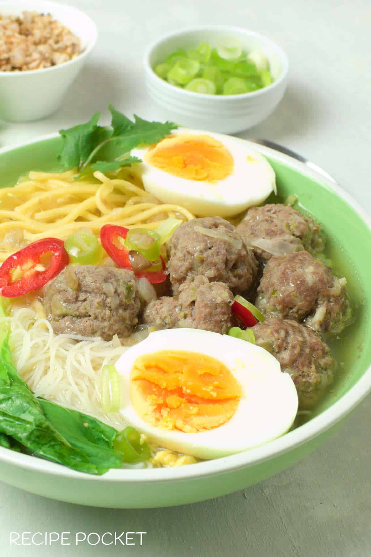 Bakso garnished with hard boiled eggs and chili.