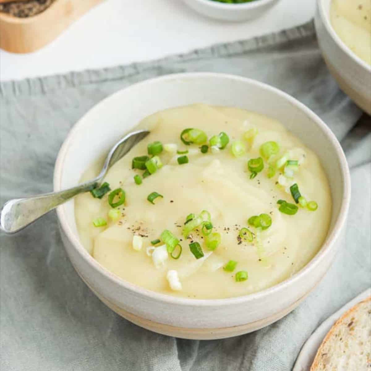 A white bowl filled with thick creamy potato soup garnished with chives.