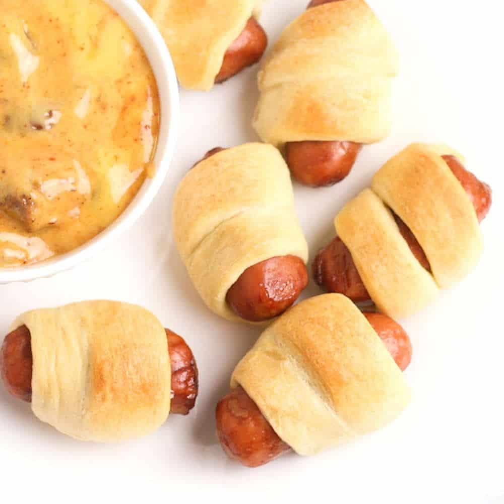 Sausages wrapped in crescent roll dough with a bowl of dipping sauce.