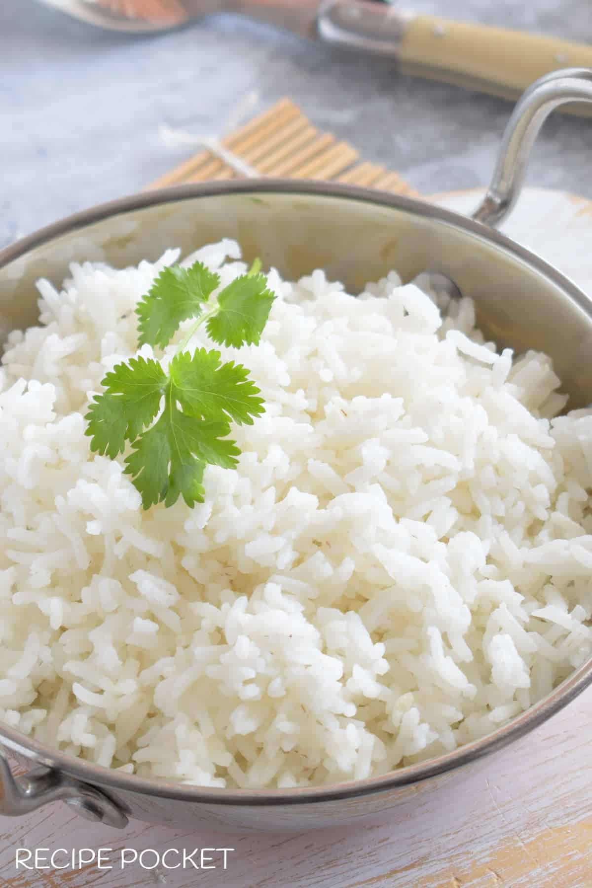 Close up of cooked basmati rice in a silver bowl with fresh coriander on top.