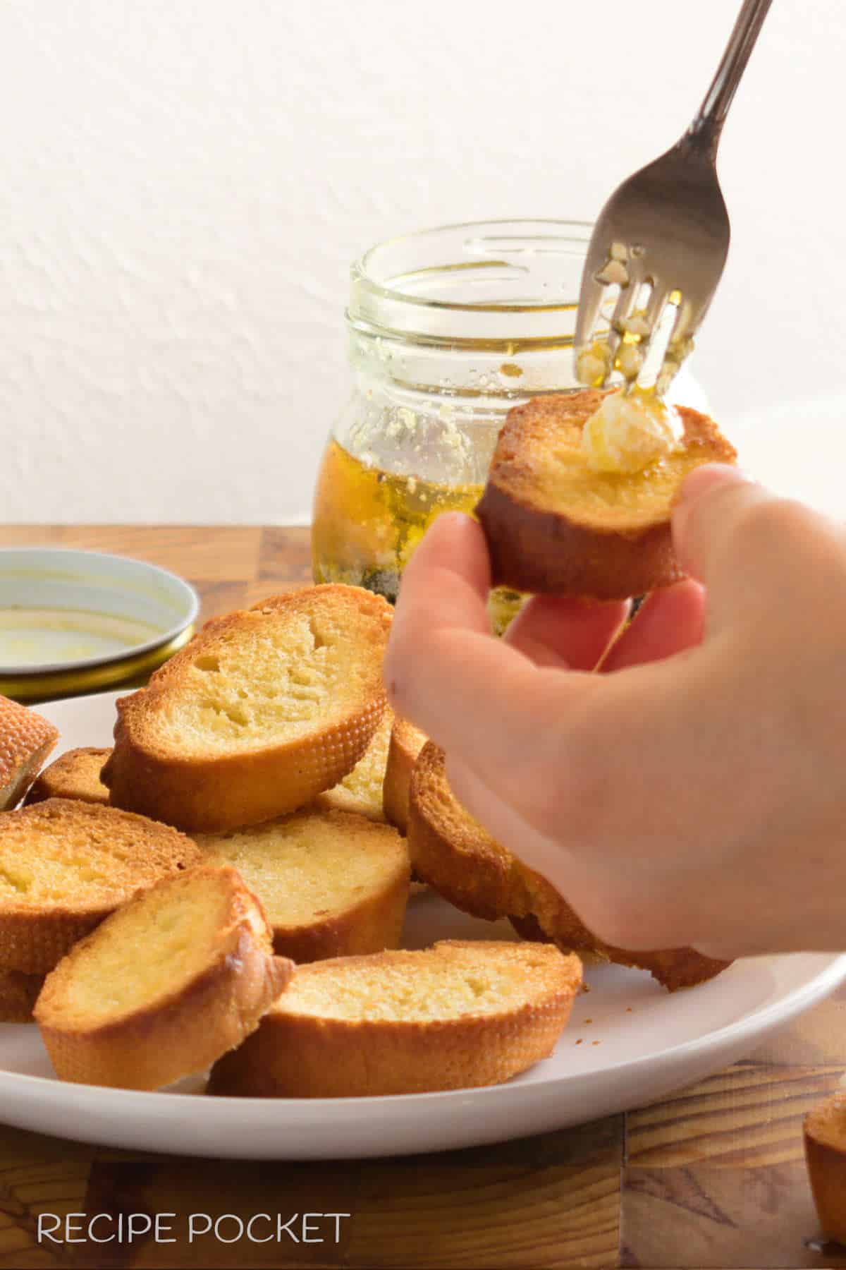A hand holding a homemade crostini over a white plate with more corostini.
