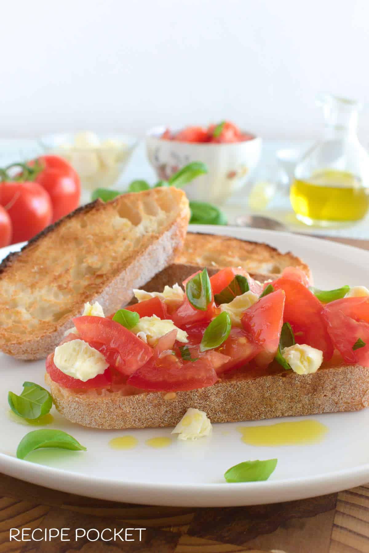 A bruschetta on a plate with two pieces of toast in the background.