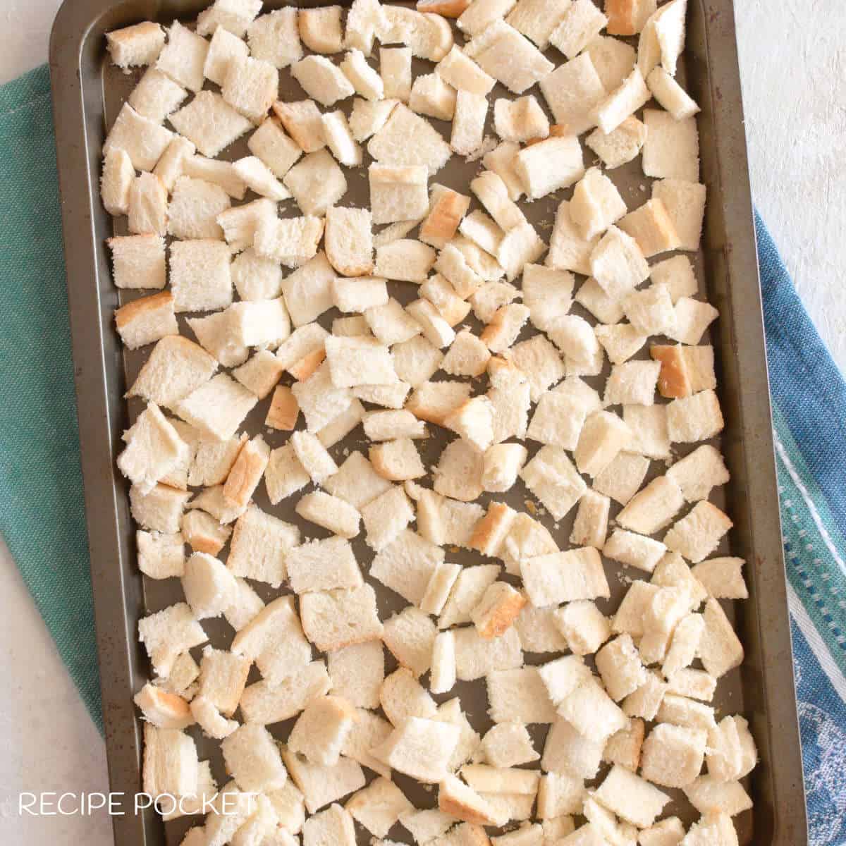 Bread cut into small cubes on a baking tray.