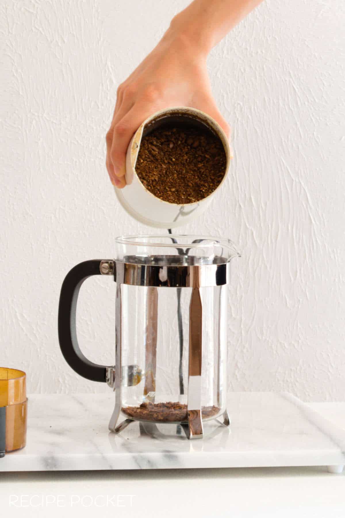 Ground coffee beans being put into a French press.