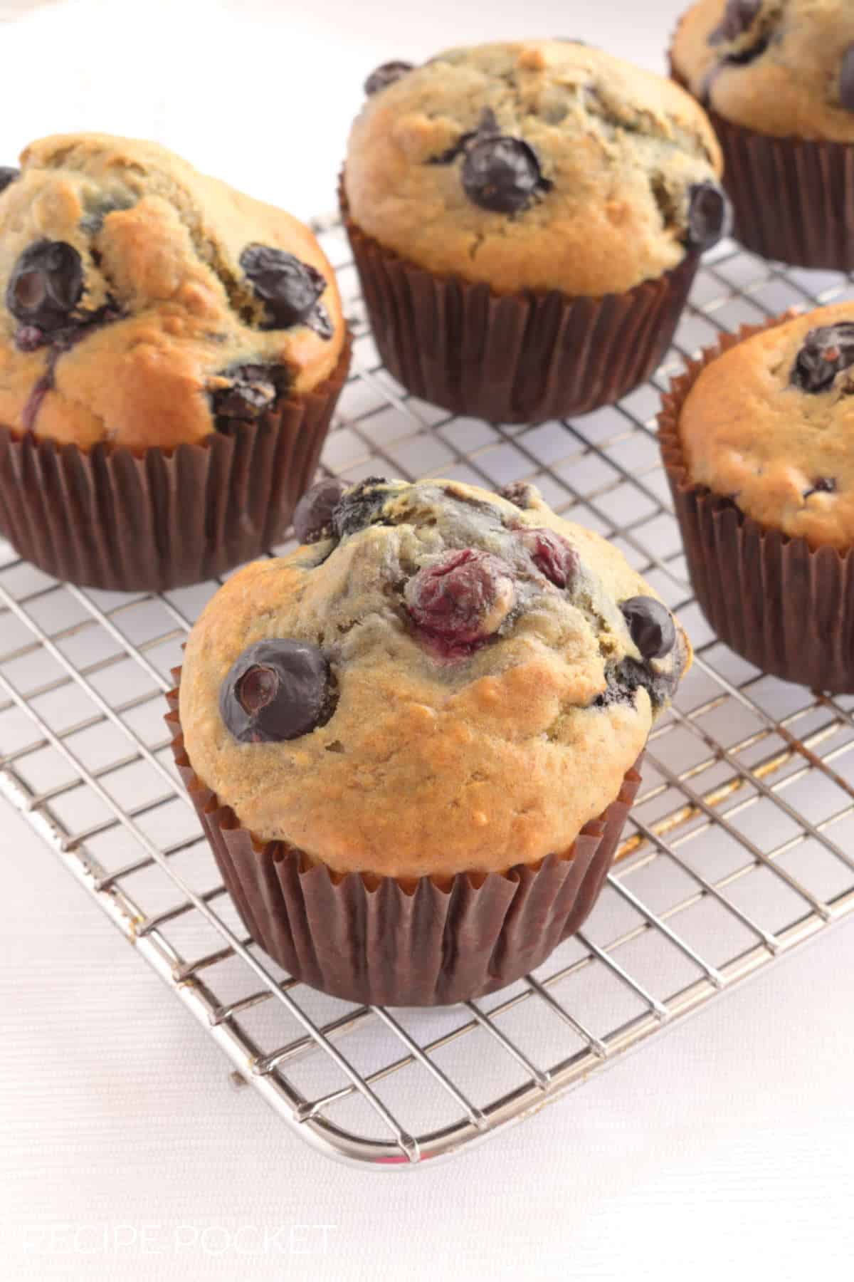 Muffins in brown wrappers on a cake rack.