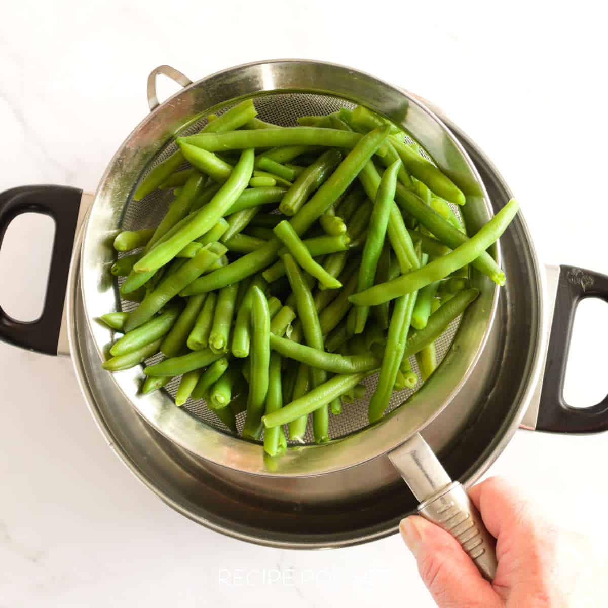 Cooked green beans in a sieve over a pot.
