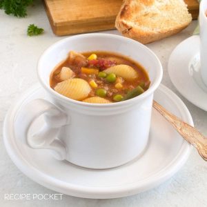 Hamburger soup in a white cup with bread in the background.