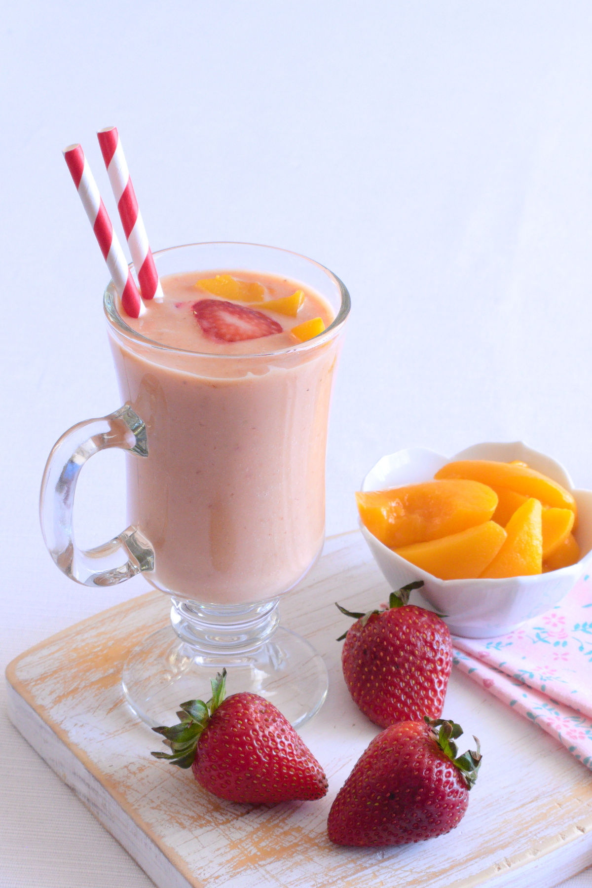 Strawberry peach smoothie in a glass with straws and fresh strawberries in the foreground.