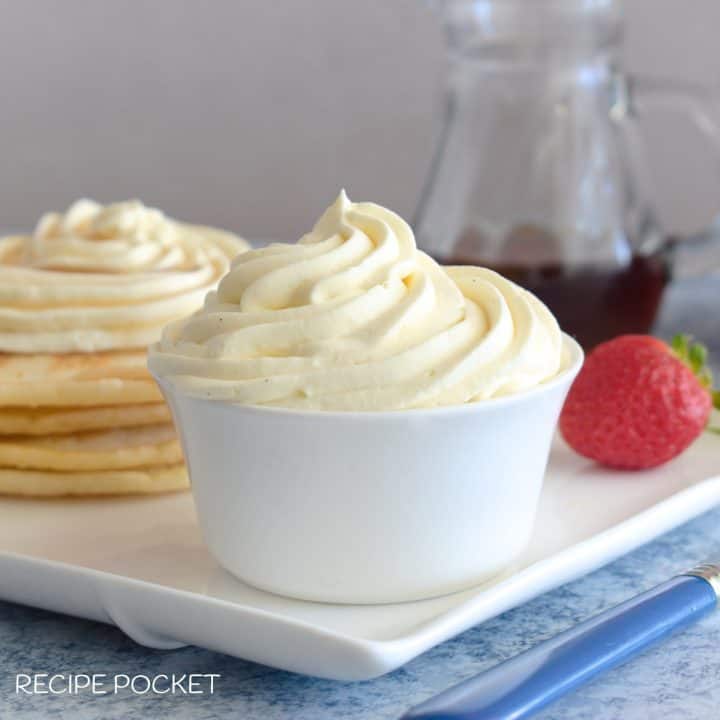 A bowl of whipped cream with pancakes in the background.