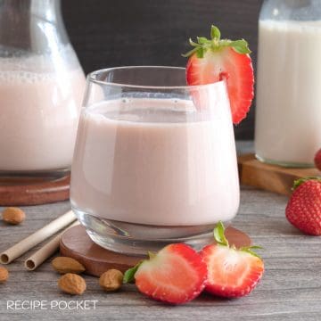 Strawberry almond milk in a glass with fresh strawberries on a table.