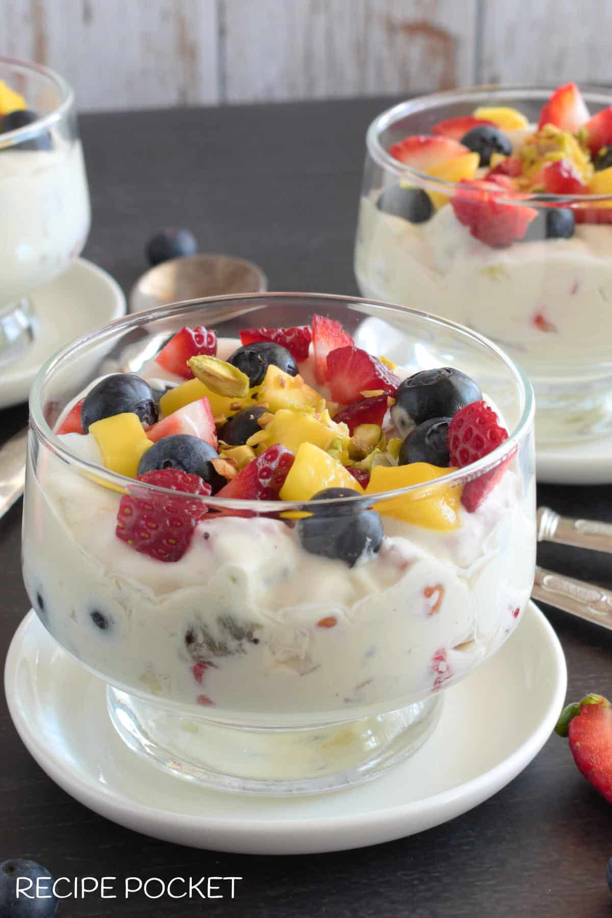 Diced strawberries, mango and blueberries in dessert bowls with cream.