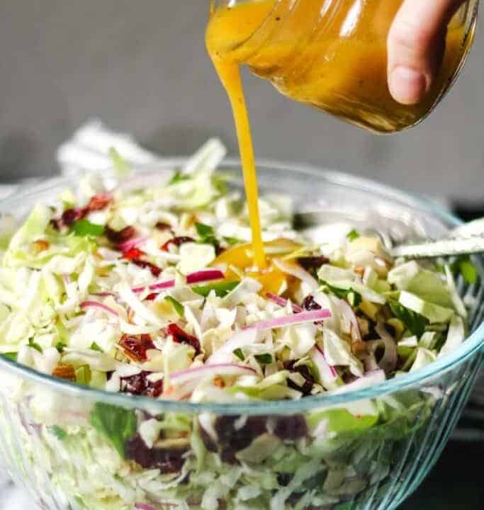 Salad dressing being poured over coleslaw.