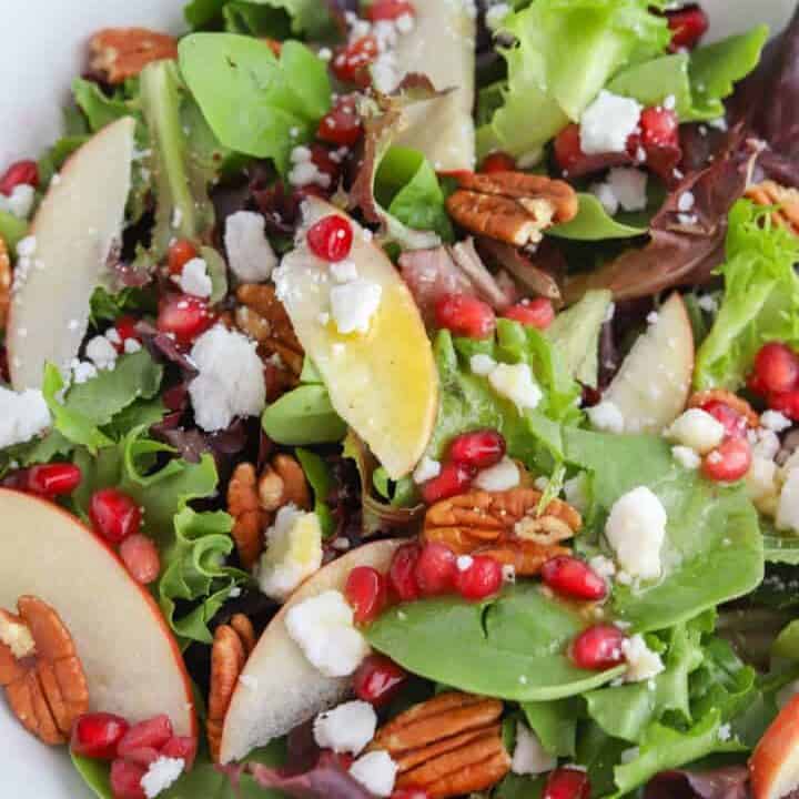 Salad made with apples, pomegrante seeds, green salad leaves and cheese.