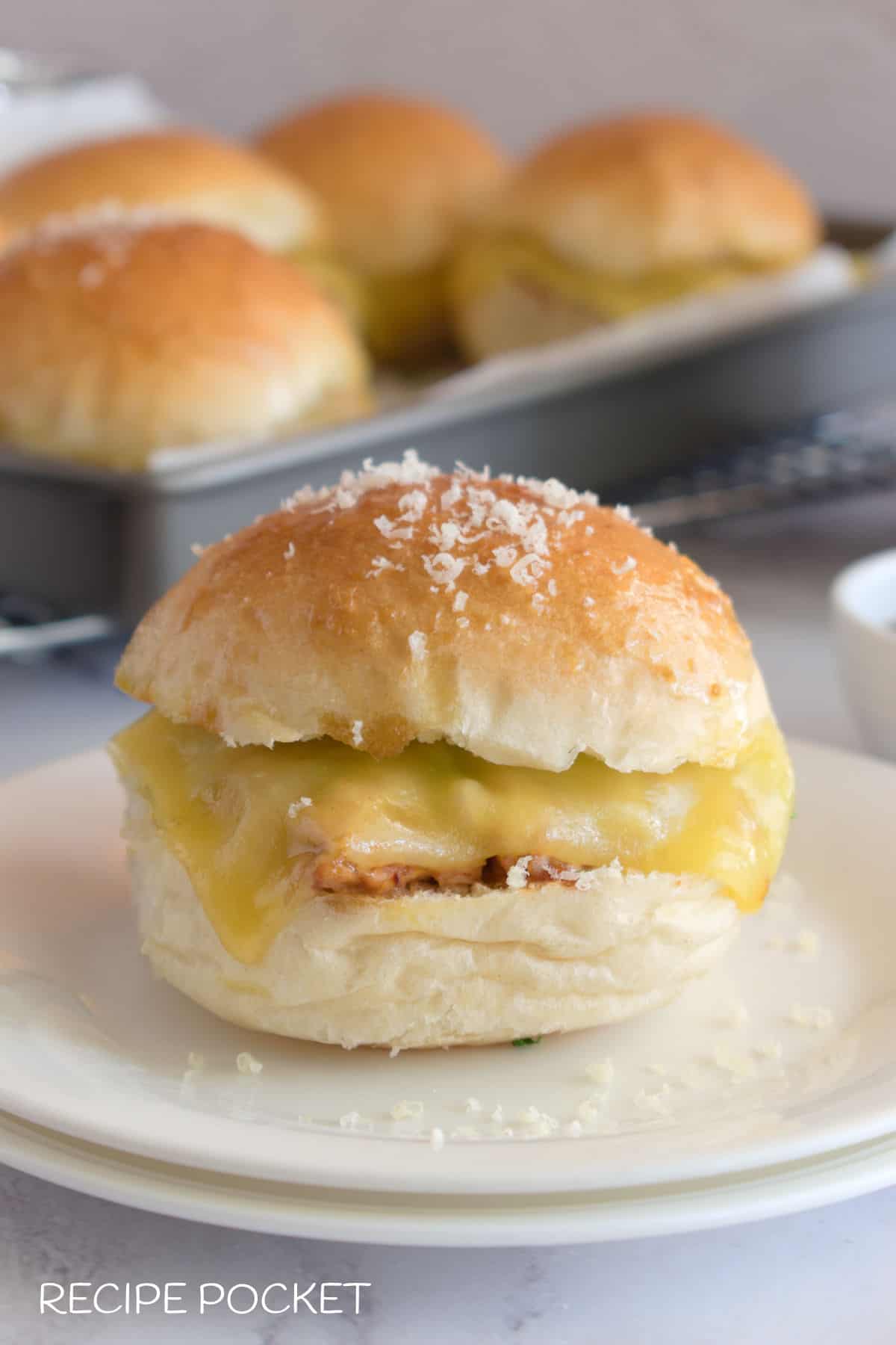 A slider on a plate with a tray of  sliders in the background.
