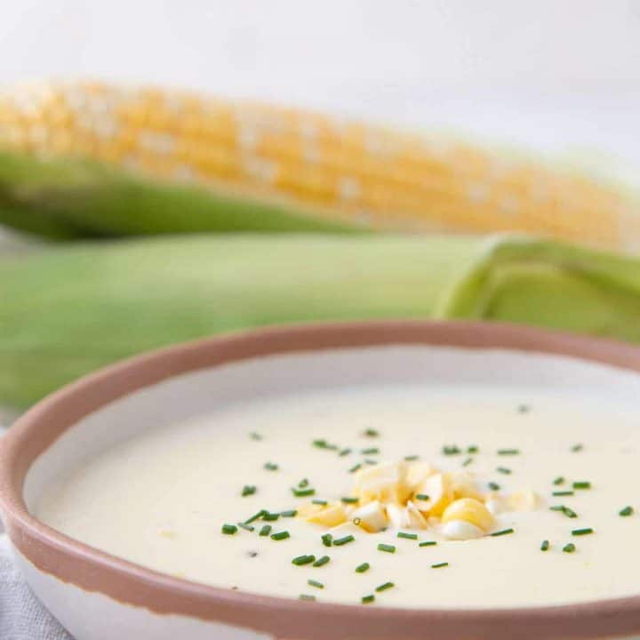 A bowl of cream of corn soup with a corn cob in the background.