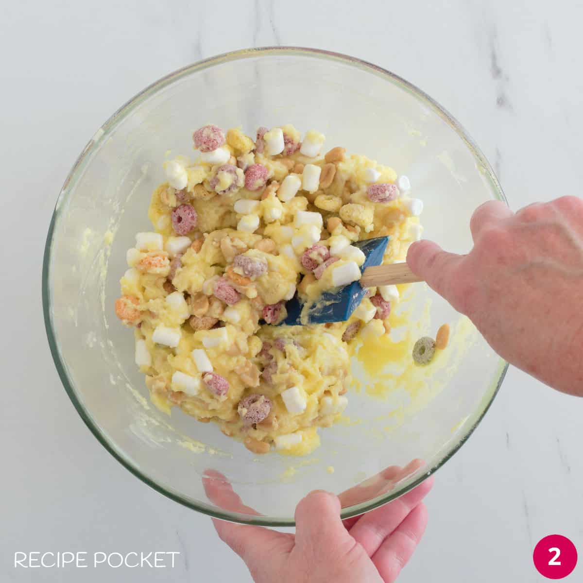 Melted white chocolate, nuts and fruit flavored cereal  being mixed in a bowl.