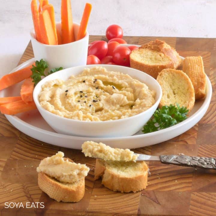 A bowl of miso hummus with crostini and vegetable sticks.