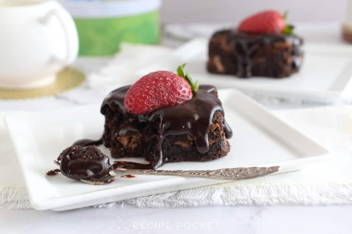 A close up of a chocolate brownie and a fork on a white plate.