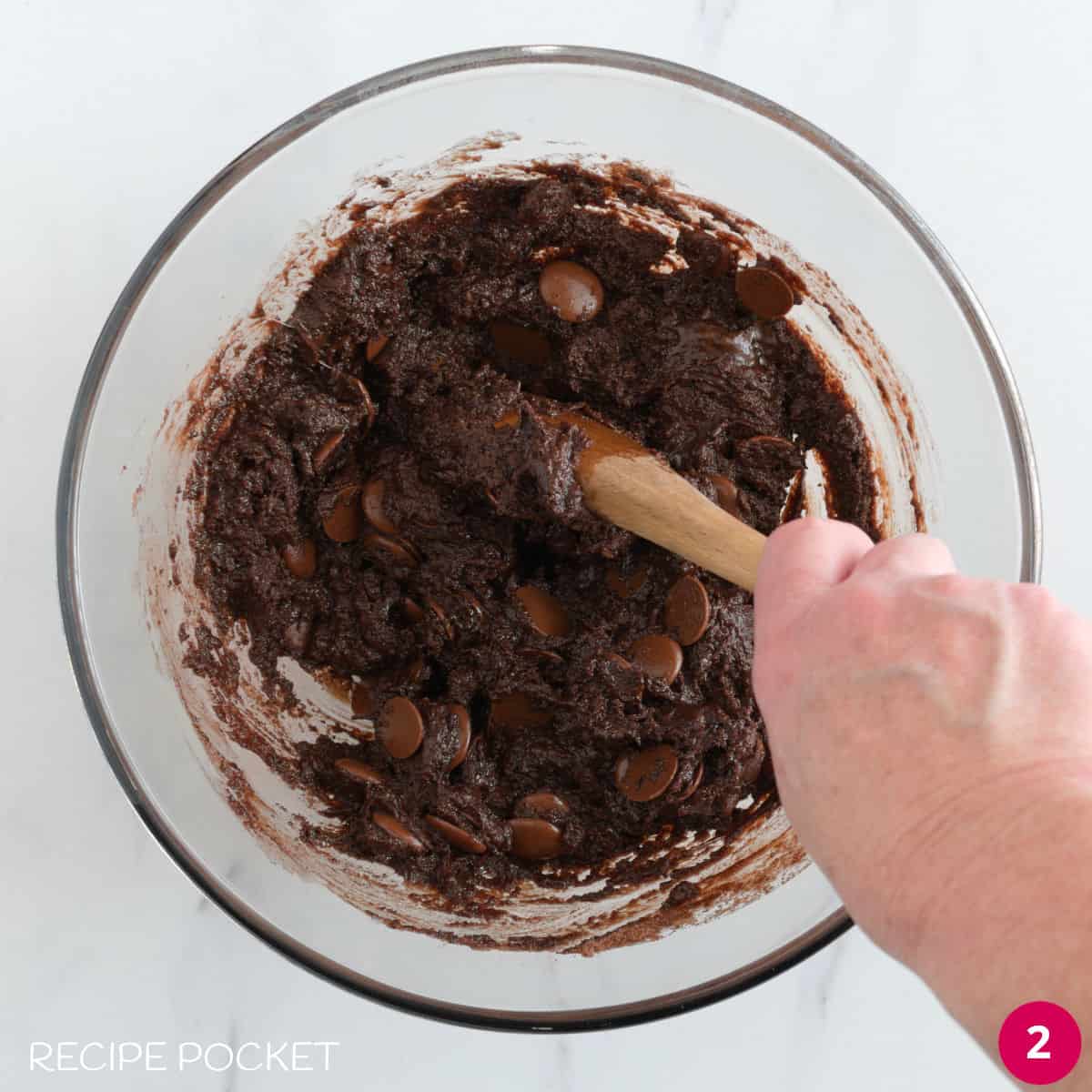 Brownie batter in a glass bowl with a wooden spoon.
