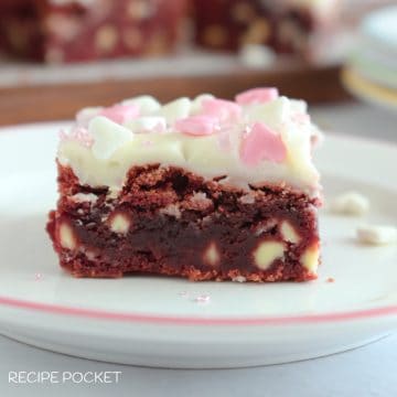 A slice of red velvet brownie with frosting on a white plate.