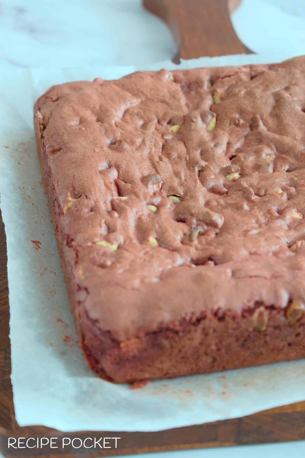 A baked brownie cake on a wooden board before frosting and cutting.