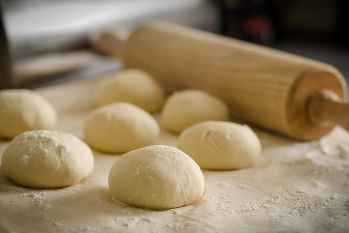 A wooden rolling pin a balls of dough and a board dusted with flour.