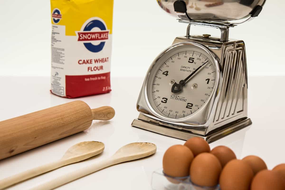 Kitchen scales, wooden spoon, eggs and a bag of flour.,