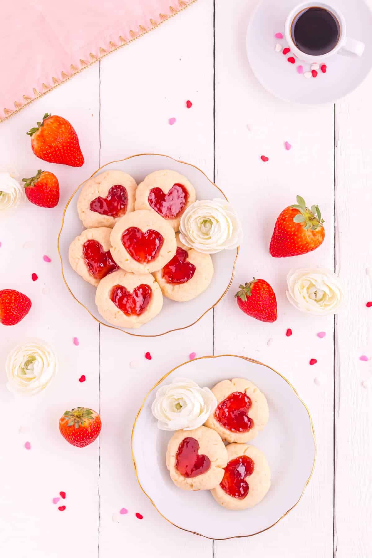 Round cookies with heart jam filled centers on white plates.