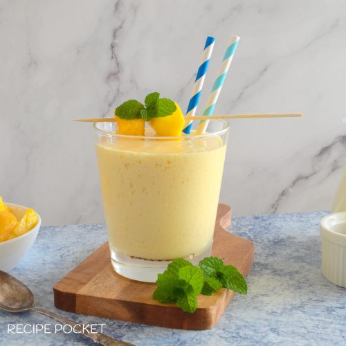 Mango shake in a glass with mint leaves in the foreground.