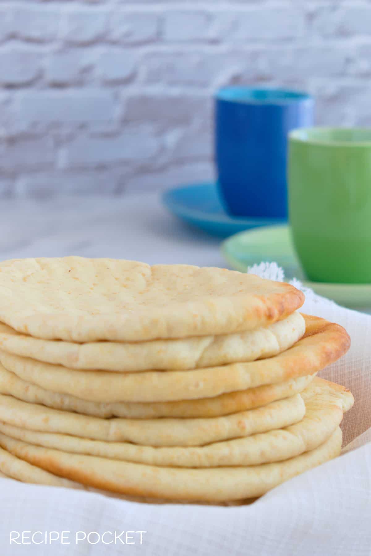 A stack of fresh pita bread on a table with blue and green mugs in the background.