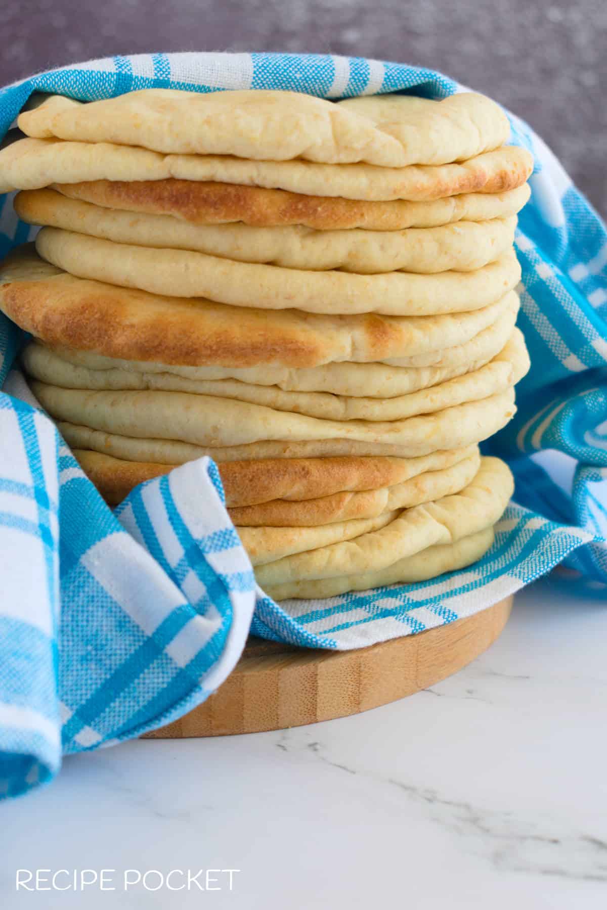 A stack of freshly made pita bread wrapped in a clean tea towel.